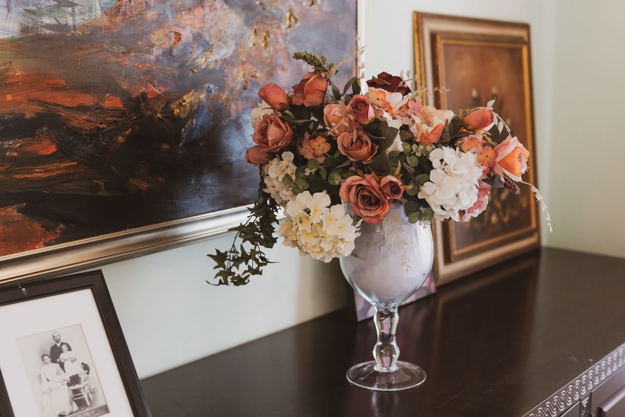 hero-img-02 Beautiful floral arrangement in a vase against a backdrop of artistic paintings, perfect for sophisticated decor.