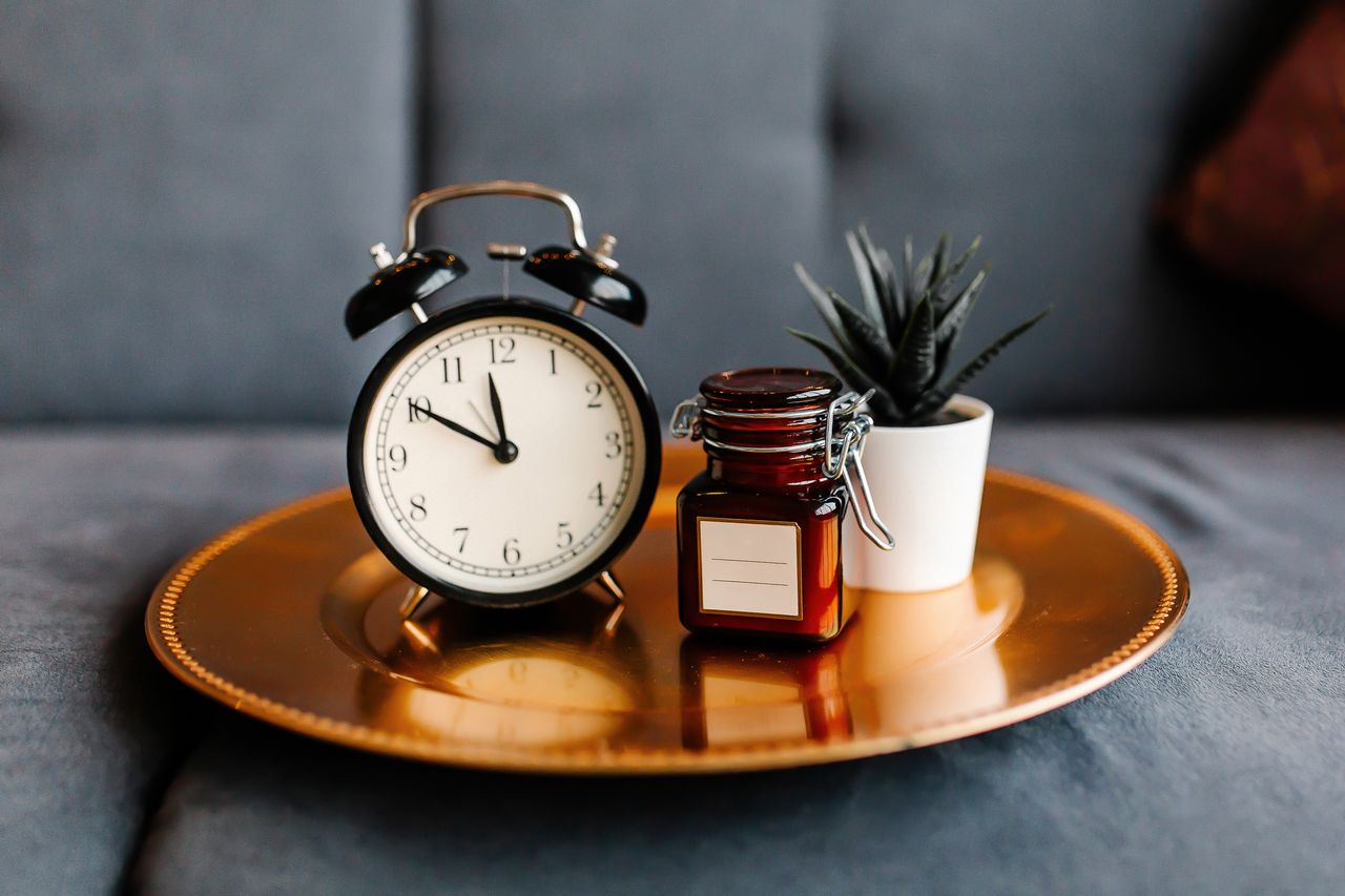 gallery-1 Aesthetic arrangement of a clock and jar on a golden tray with a potted plant.
